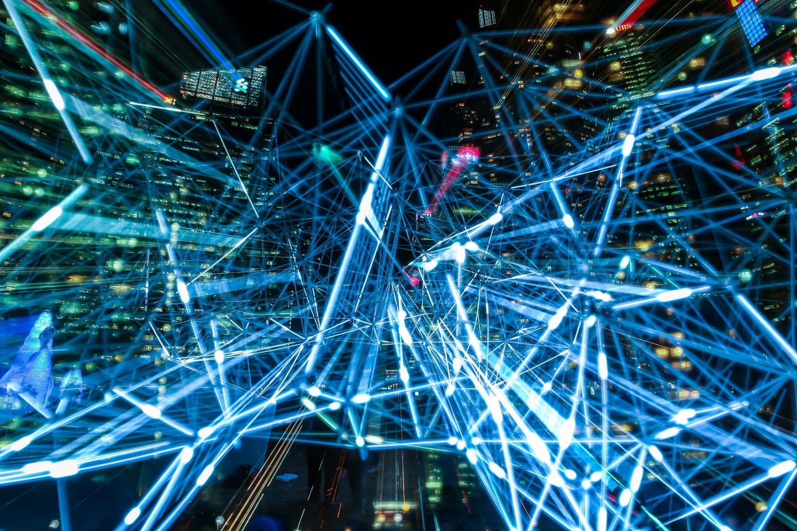 Long-exposure photograph of blue light trails forming a dense web across city buildings at night