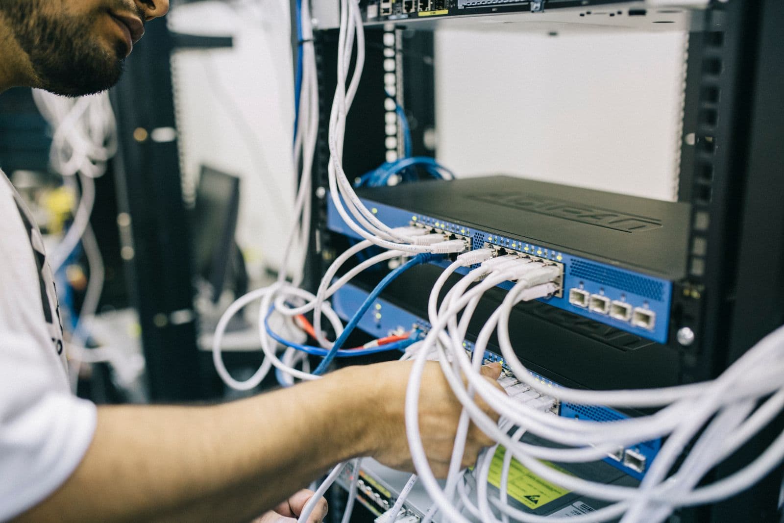 A technician connecting white network cables into a rack-mounted switch inside a server cabinet