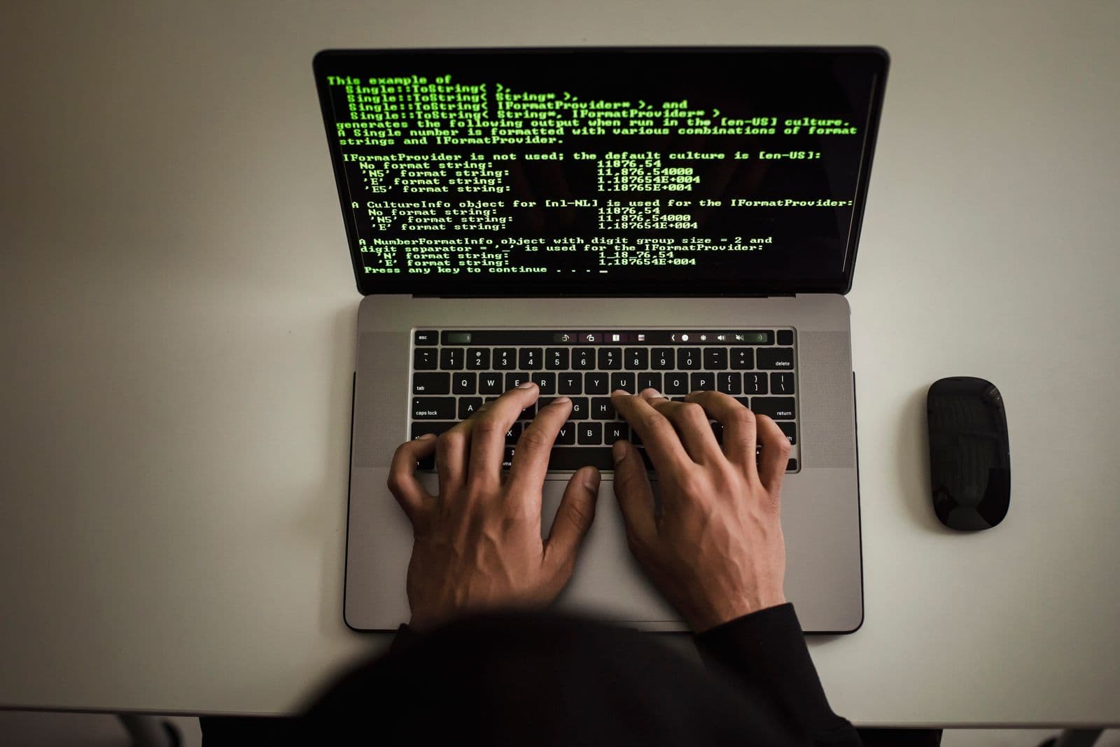Overhead view of two hands typing on a laptop keyboard, the screen filled with green terminal text