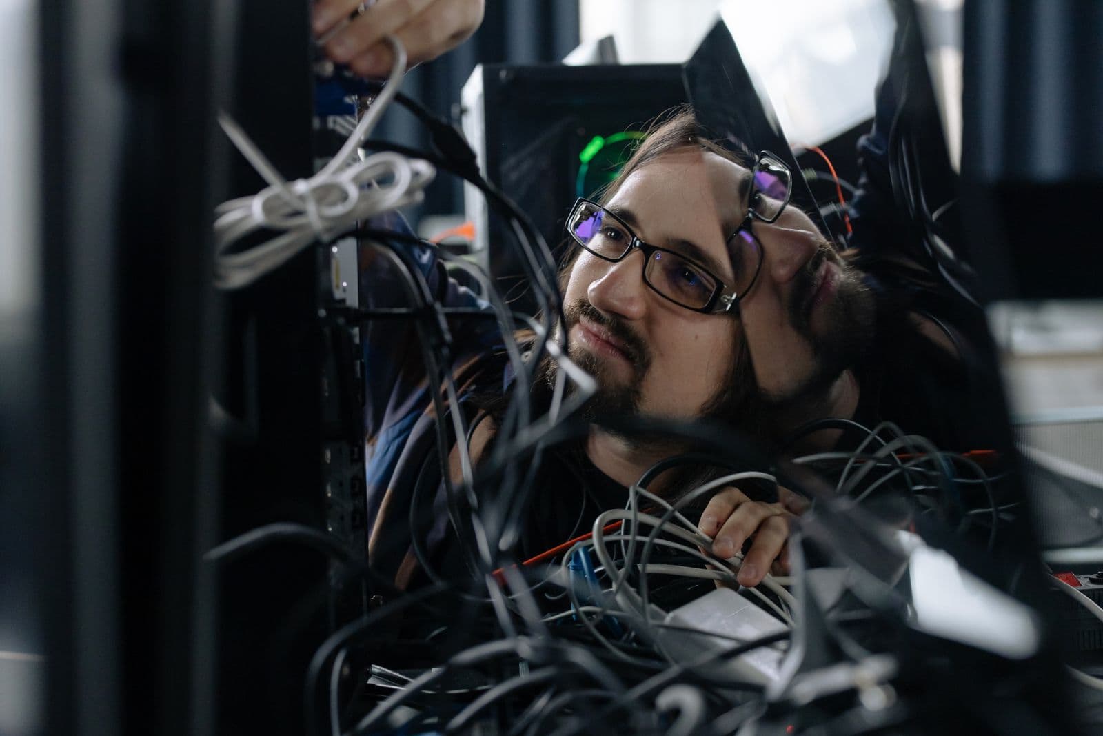 Employee untangling a mess of network cables behind an office computer workstation